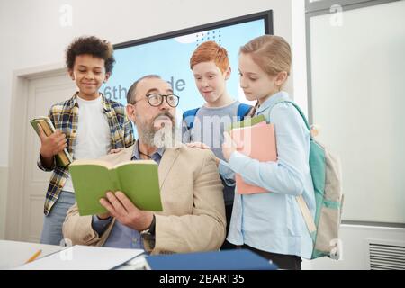 Low angle view at multi-ethnic group of children standing around bearded senior teacher in school classroom Stock Photo