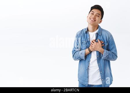 Portrait of touched handsome taiwanese man in love, express sympathy and passionate feelings towards girlfriend, being touched, hold hands pressed to Stock Photo