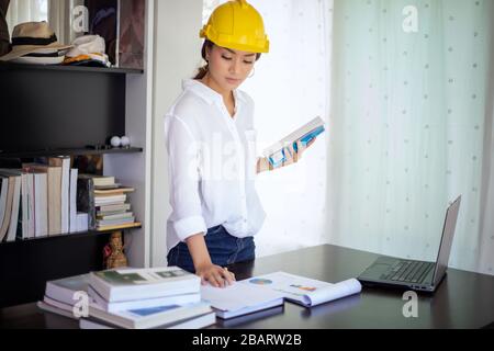 Beautiful Asian engineering women checking document and using notebook working from home for social distance and self responsibility concept Stock Photo