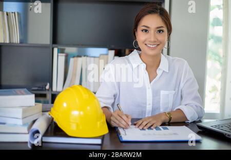 Beautiful Asian engineering women checking document and using notebook working from home for social distance and self responsibility concept Stock Photo