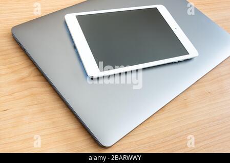 A white tablet and a laptop computer on a wooden surface. Stock Photo