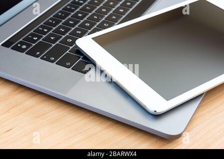 A white tablet and a laptop computer on a wooden surface. Stock Photo