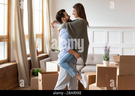 Strong affectionate young man in glasses lifting smiling wife. Stock Photo