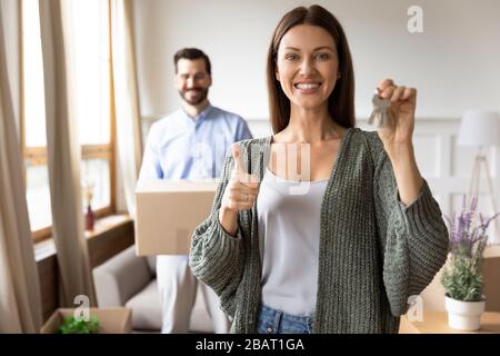 Overjoyed young 30s woman holding keys, showing thumbs up gesture. Stock Photo