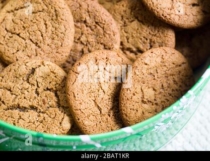 Freshly baked ginger snap cookies: A tin of freshly baked ginger cookies piled haphazardly in a round green cookie tin. Stock Photo