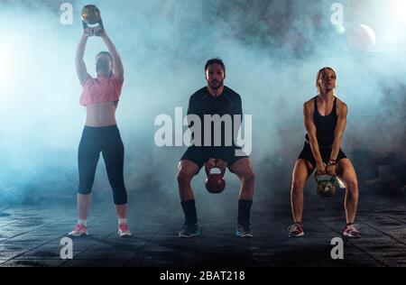 Group of athletes swinging a kettle bell over their head in crossfit gym Stock Photo