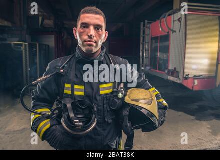 Portrait of a fireman wearing firefighter turnouts holding helmet ready for emergency service. Stock Photo