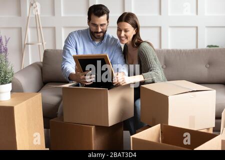 Happy young family couple unpacking belongings, looking at family photo. Stock Photo