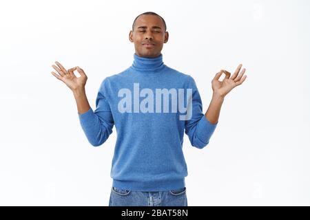 Portrait of calm and patient young african-american man self-isolating at home during pandemia, reaching nirvana during meditating, relaxing with yoga Stock Photo