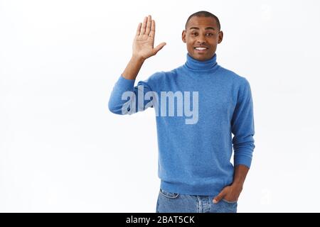 Portrait of friendly charismatic young african-american man saying hi to people at work, raising hand and waving it hello, informal greeting sign Stock Photo