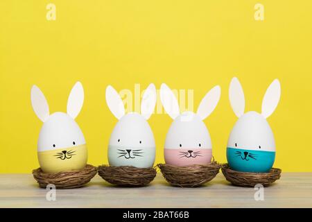 Easter eggs with bunny faces in nest on a yellow background with space for copy Stock Photo