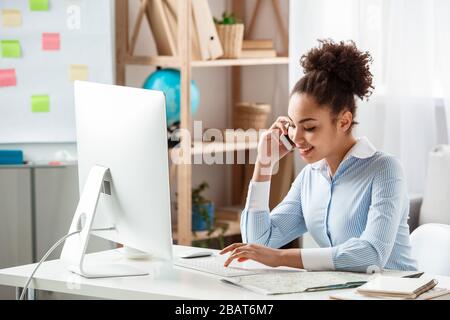 Tour agent sitting at table in office answering phone call using computer joyful Stock Photo