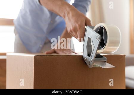 Young man using adhesive scotch, packing carton box at home. Stock Photo