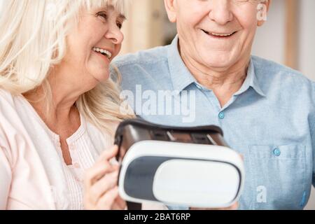 Senior couple sitting in travel agency holding virtual reality headset laughing close-up Stock Photo