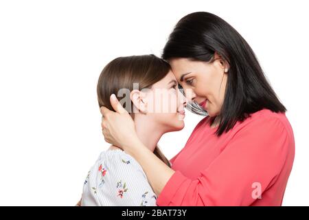 Waist up studio portrait of a young mother embracing her cute schoolgirl daughter. Happy smiling family background isolated over white background. Stock Photo