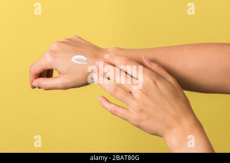closeup of tender hands of a young woman with moisturizer on against yellow background. spring skin protection Stock Photo