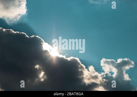 hope is not lost. sun rising under dark clouds against blue sky Stock Photo