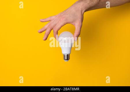 close up man hand holding white led light bulb against yellow background. concept of creativity, inspiration and new ideas Stock Photo