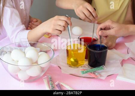 Children interfere with a solution with food coloring in glasses to paint Easter eggs Stock Photo