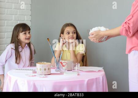 Mom brought a large plate with eggs to the girls on the table, for their subsequent painting by Easter Stock Photo