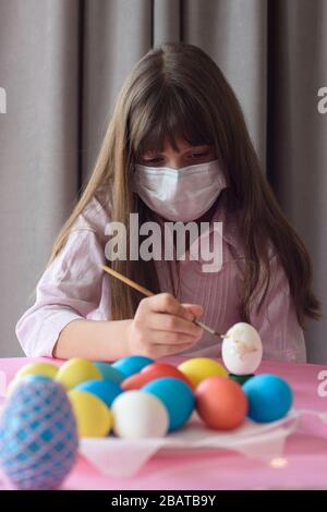 Sad quarantined girl paints Easter eggs with a brush Stock Photo