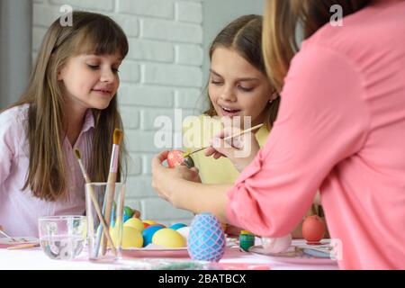 Mom shows girls how to paint Easter eggs beautifully Stock Photo