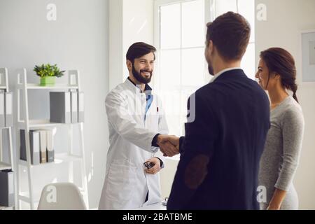 Confident doctor and couple patient sitting at the table in clinic office. Family doctor. Stock Photo