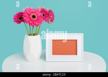 Happy Mother's Day, Women's Day, Valentine's Day or Birthday Background. Beautiful dark pink gerbera daisies in a vase and an empty picture frame gree Stock Photo