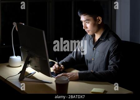 Young adult asian businessman and woman working late at night in their office with desktop computer and laptop. Using as hard working and working late Stock Photo