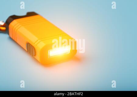 Orange led Flashlight with a carabiner on a blue background. LED lights in flight. Stock Photo