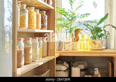 Food storage at home, sunflower oil on table in pantry. Pantry interior, wooden shelf with food cans and kitchen utensils Stock Photo