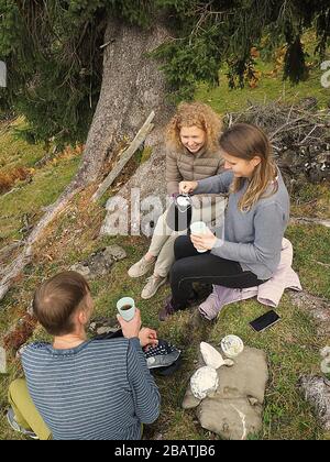 Young group of 3 upon a mountain after hiking having a break with tee and coffee Stock Photo