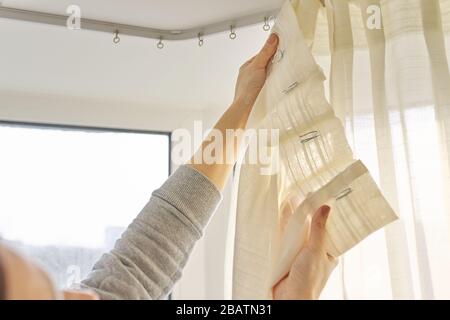 Close up of woman hands hanging curtain with metal hooks on ceiling ledge. Stock Photo