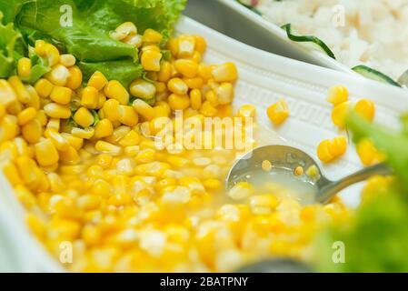 Organic Yellow Steamed Corn in a Bowl. Close up of cooked sweet corn seeds in a red bowl on a wooden table. Selective focus. Stock Photo