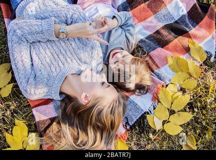 Top view young mother lying with her little daughter on blanket and smiling while having fun in autumn park. Tiny girl playing with her mom while layi