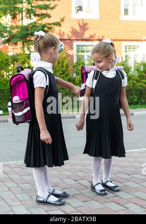 Schoolgirls with backpacks ready back to school. Two twin sisters outdoor Stock Photo