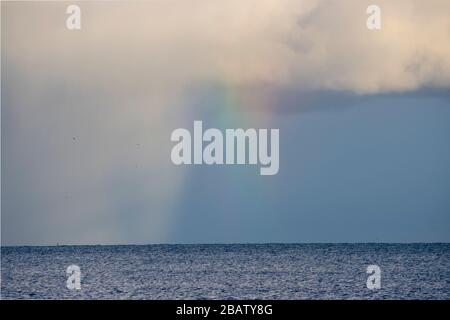 A rainbow appears as sun shines through rain clouds across the sea Stock Photo