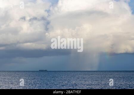 A rainbow appears as sun shines through rain clouds across the sea Stock Photo
