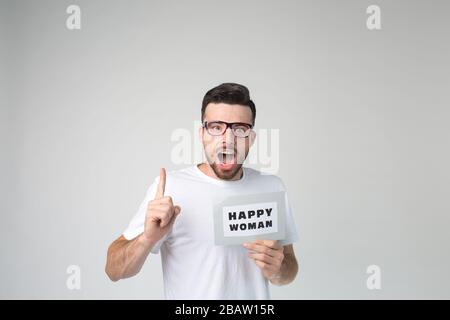 Young man isolated over background. Emotional guy teaches about woman happiness. Hold big thumb up. Guy look straight through glasses. Alone in studio Stock Photo