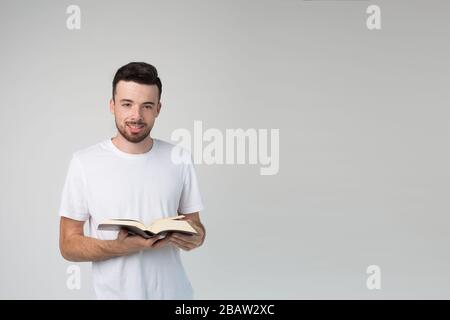 Young man isolated over background. Nice handsome positive guy hold book in hands and look on camera with smile. Wise smart man in studio. Stock Photo