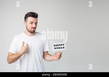 Young man isolated over background. Self-confident brutal guy pointing on himself. Hold paper with happy woman words on it. Self-assured guy on Stock Photo