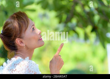 Side face of a beautiful woman healthy middle-aged Asian people dress in Thai style clothes, Portrait old lady relaxing outdoors pointing finger looki Stock Photo