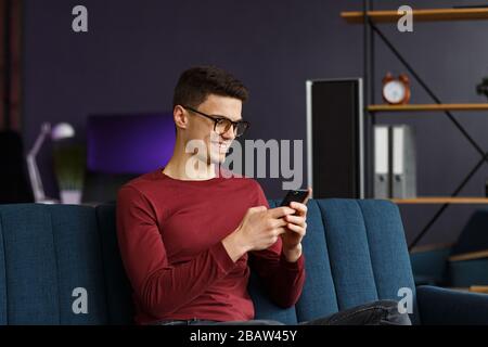 Young freelancer using smartphone and smiling. Happy man using m Stock Photo