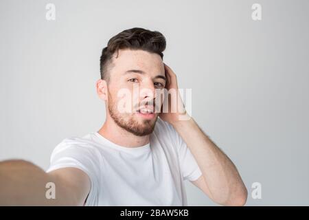 Young man isolated over background. Guy hold camera and take selfie. Posing alone with pleasure. Hold one hand on ear. Mysterious and emotional. Stock Photo