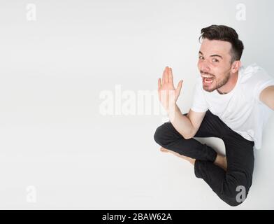 Young man isolated over background. Guy sit on floor and wave with hand. Take selfie or picture alone. Side view of expressive man. Stock Photo