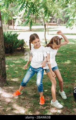 Two little girls in white t-shirts having fun in park outdoor. Stock Photo