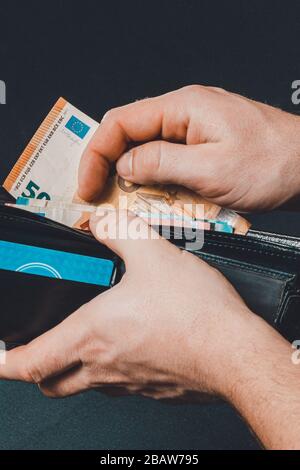 Closeup of human hands putting euro banknotes in wallet isolated on black background. Stock Photo