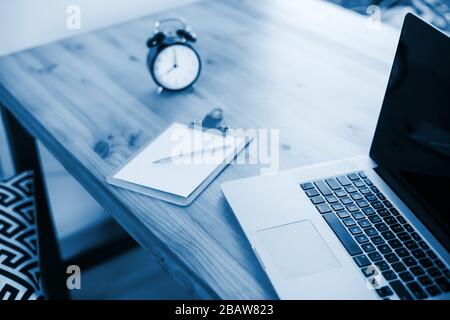 Comfortable working place in home office with wooden table and modern laptop laying on it. Freelance work concept. Color of the year 2020 classic blue Stock Photo