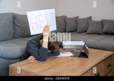 Learning difficulties. Sad tired frustrated boy sitting at the table with many books and holding paper with word Help. Education concept. Stock Photo