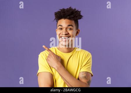 Close-up portrait of cheerful, attractive young male student showing promo, pointing at upper left corner, smiling pleased, recommend click link Stock Photo